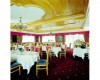 Elegantní restaurace s kulatými stoly, pokrytými bílými ubrusy, a luxusním dřevěným stropem.